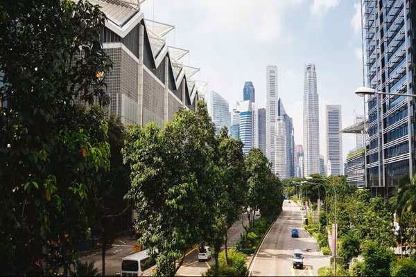 A sustainable, green-designed urban streetscape featuring a multi-lane roadway flanked by dense tree-lined medians, pedestrian pathways, modern eco-friendly architecture, and skyscrapers in the background