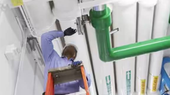 A mechanic perched on a step-stool, fixing a pipe