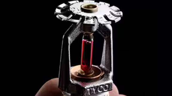 A person holding a fire sprinkler against a black background