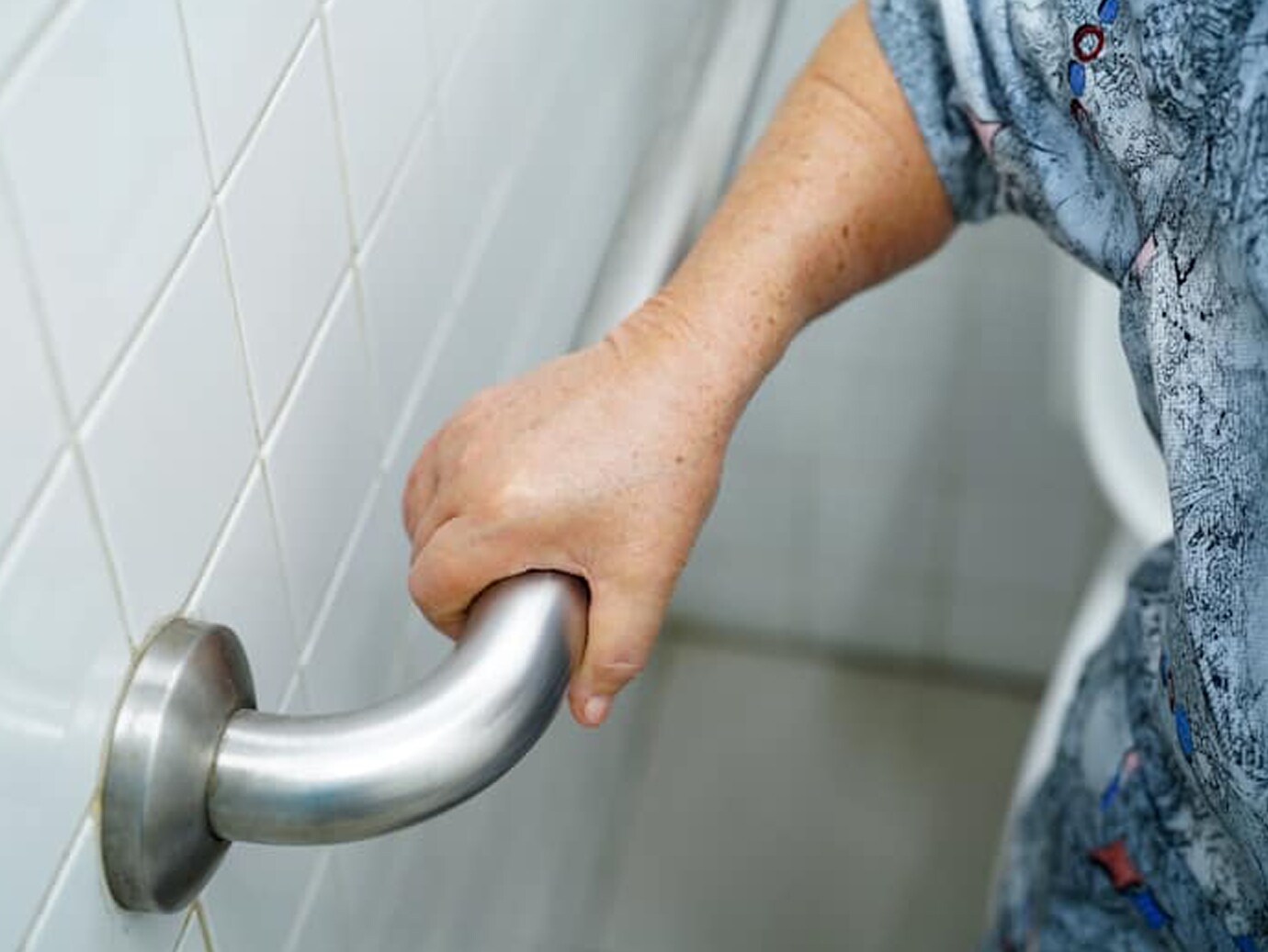 Close-up of an elderly person holding a hand-rail in a restroom