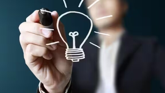 A hand drawing a lightbulb on the screen