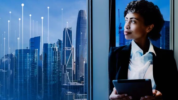 A businesswoman holding a tablet and looking at a city view through the window