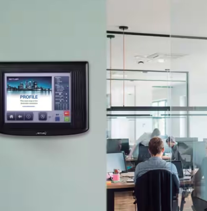 A control panel installed on a wall next to a room with people working inside
