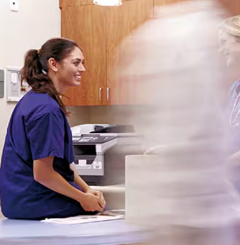 Two female hospital nurses smiling at each other while a doctor walks by them