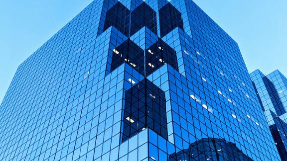 A corporate building with blue glass windows, against a blue sky