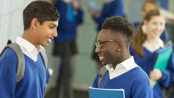 Two schoolboys smiling and conversing, while other students walk behind them