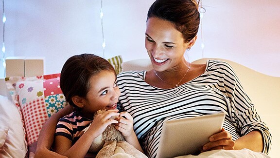 Mother and daughter looking at each other sitting in bed with a tablet in hand