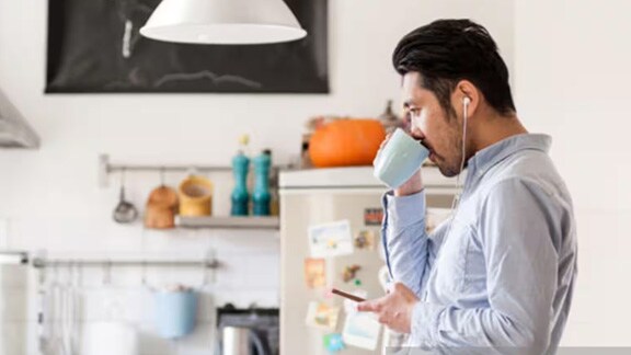 Man with earphones in and a phone in his hand drinking out of a mug
