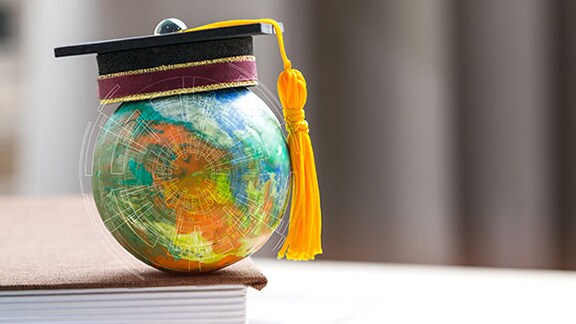 A miniature globe with a graduation hat stacked on a book