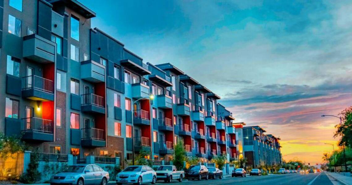 An apartment complex with cars parked in front across a road during dusk