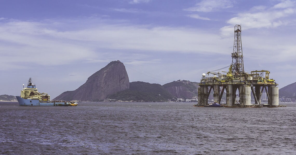 An oil tanker moving towards an oil rig with hills in the background