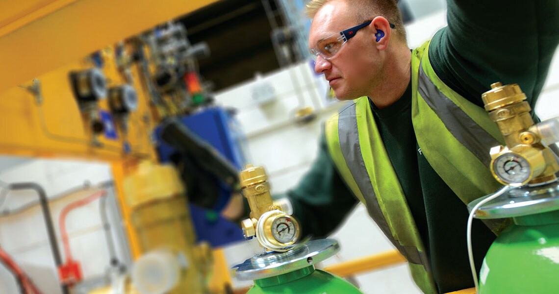 A man in safety equipment with green fire extinguishers in the foreground