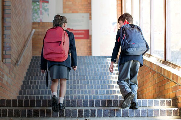 Two children in school uniforms walking up a staircase