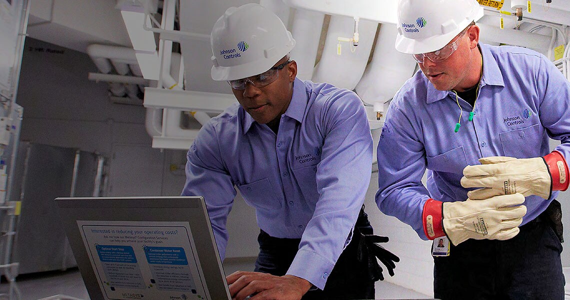 Two people in Johnson Controls safety equipment looking at a laptop