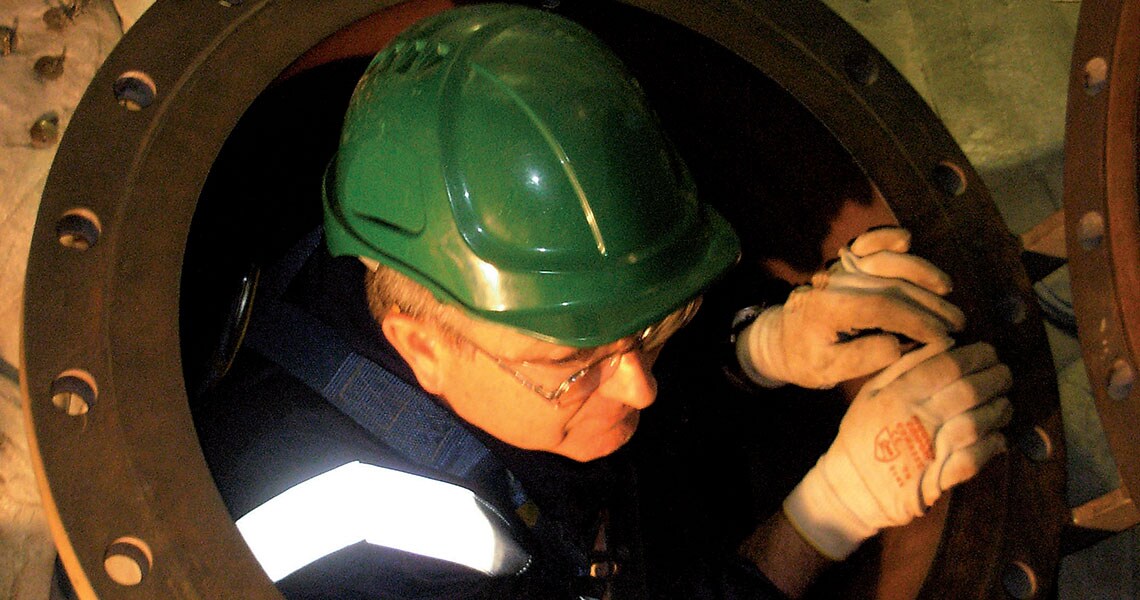 A man in safety gear coming out of a manhole cover