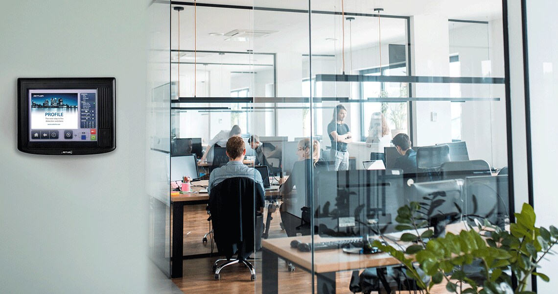 A fire control panel on a wall next to an office with people working inside