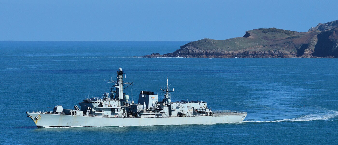 A ship sailing in ocean with a cliff in the background