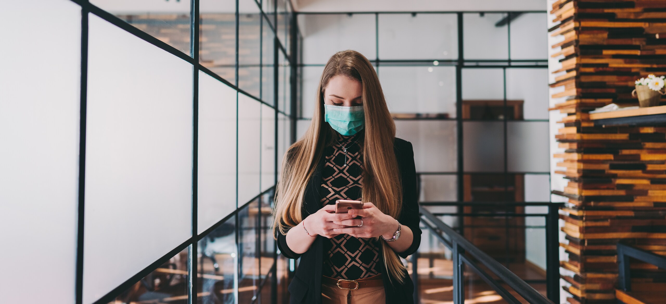 Woman in a surgical face mask using a smartphone in office