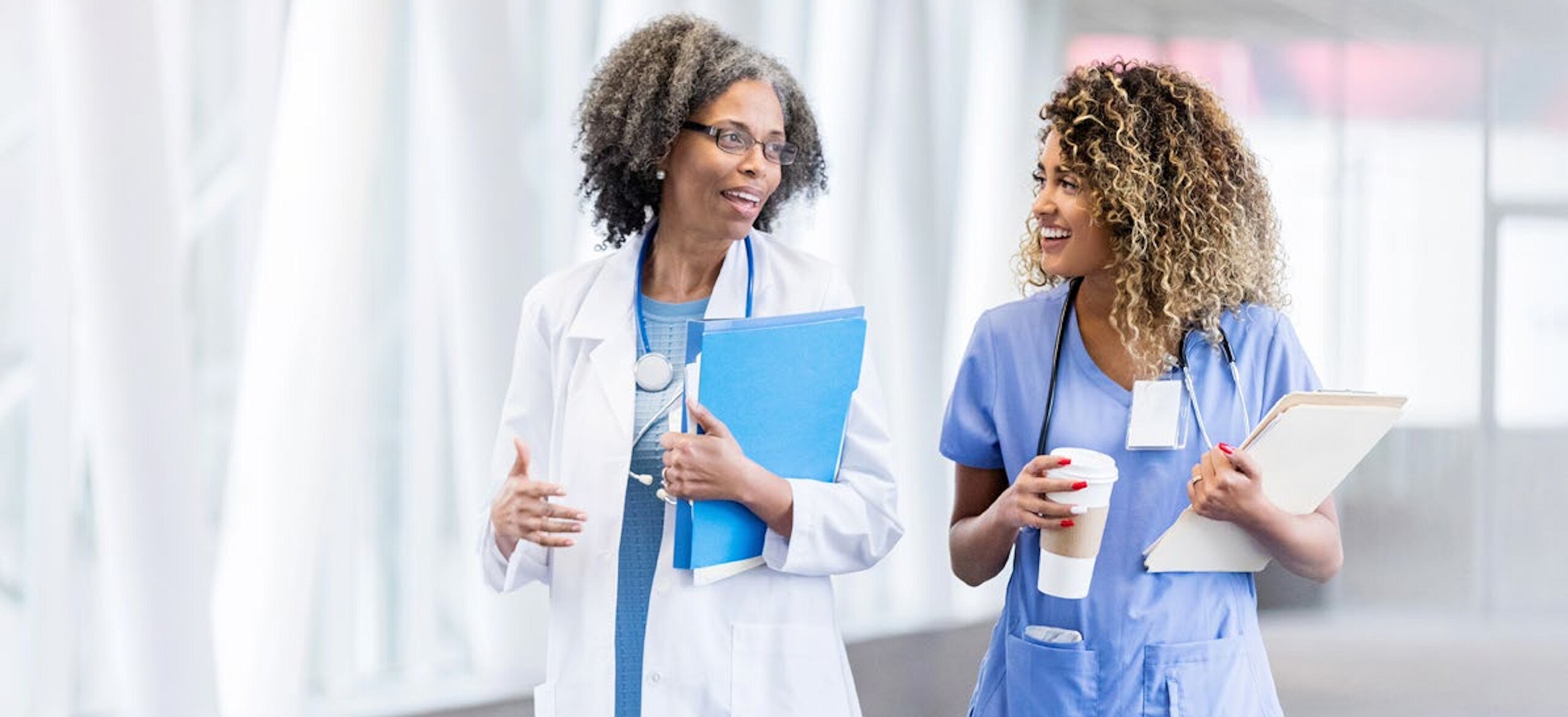 Two female healthcare workers walking down a hospital corridor while chatting