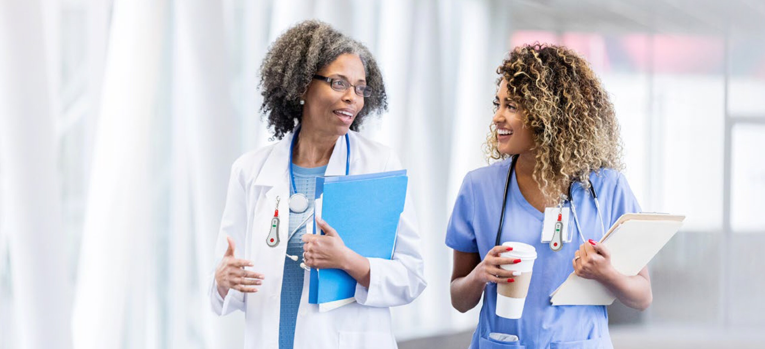 Two medical staff walking with clipboards having a conversation