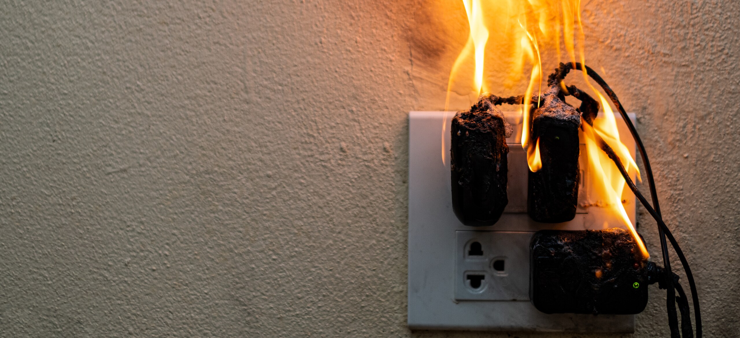 An electrical fire starting out of a socket with three plugs plugged in