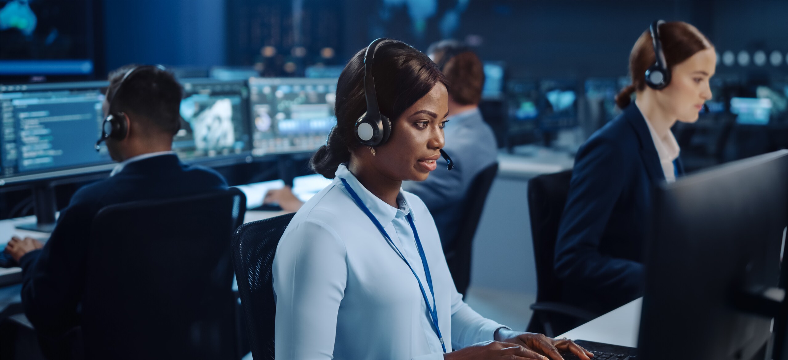People sitting in front of computers wearing headphones with mics