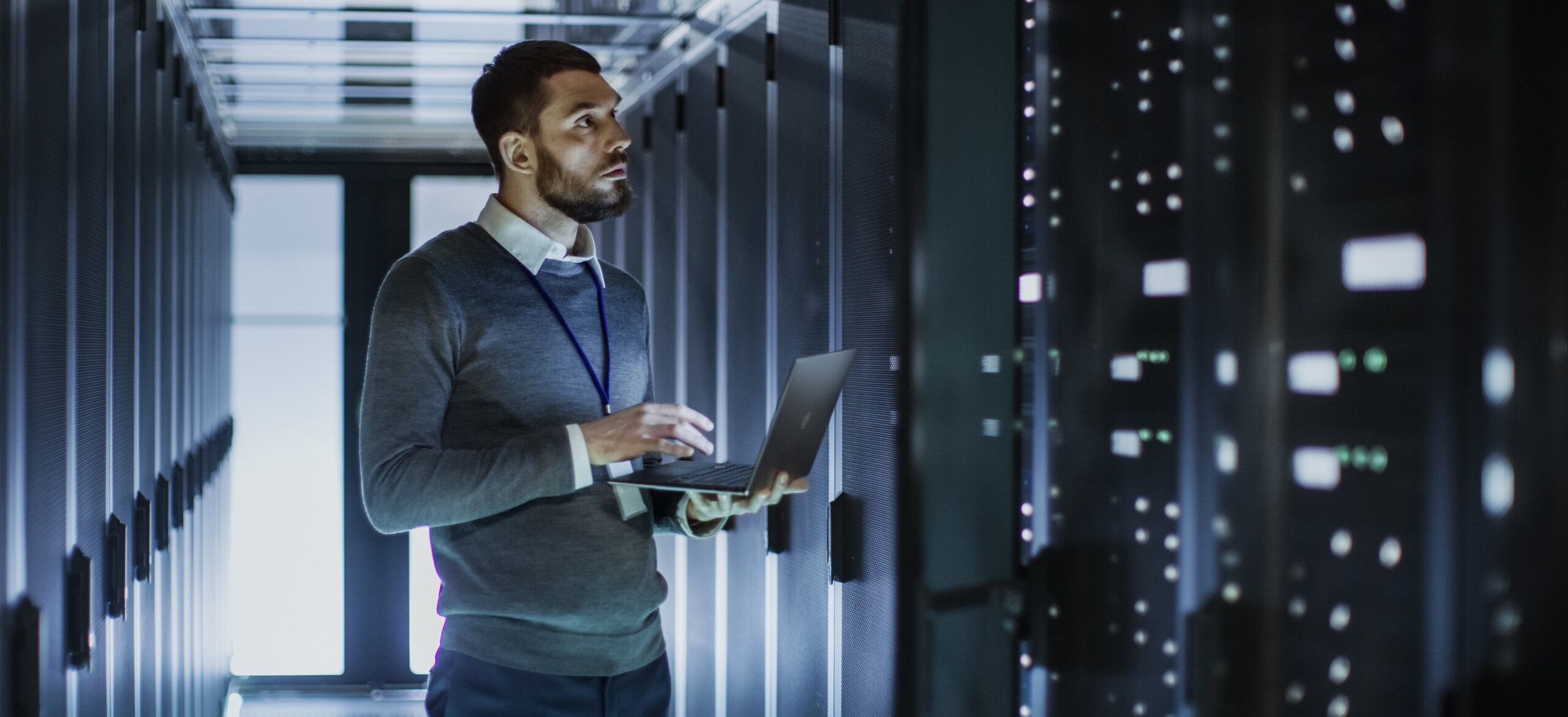 A man holding a laptop looking at a data rack in a data centre