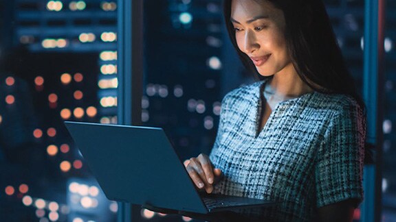 A woman working on her laptop while standing against a window