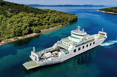 Container ship carrying trucks on water surrounded by greenery