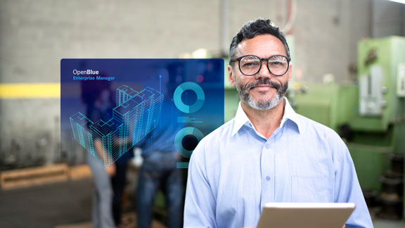 Smiling businessman with a tablet in his hands with an overlaid image of OpenBlue Enterprise Manager window in the background