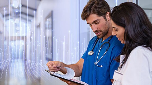Two healthcare professionals in conversation, while one holds a clipboard