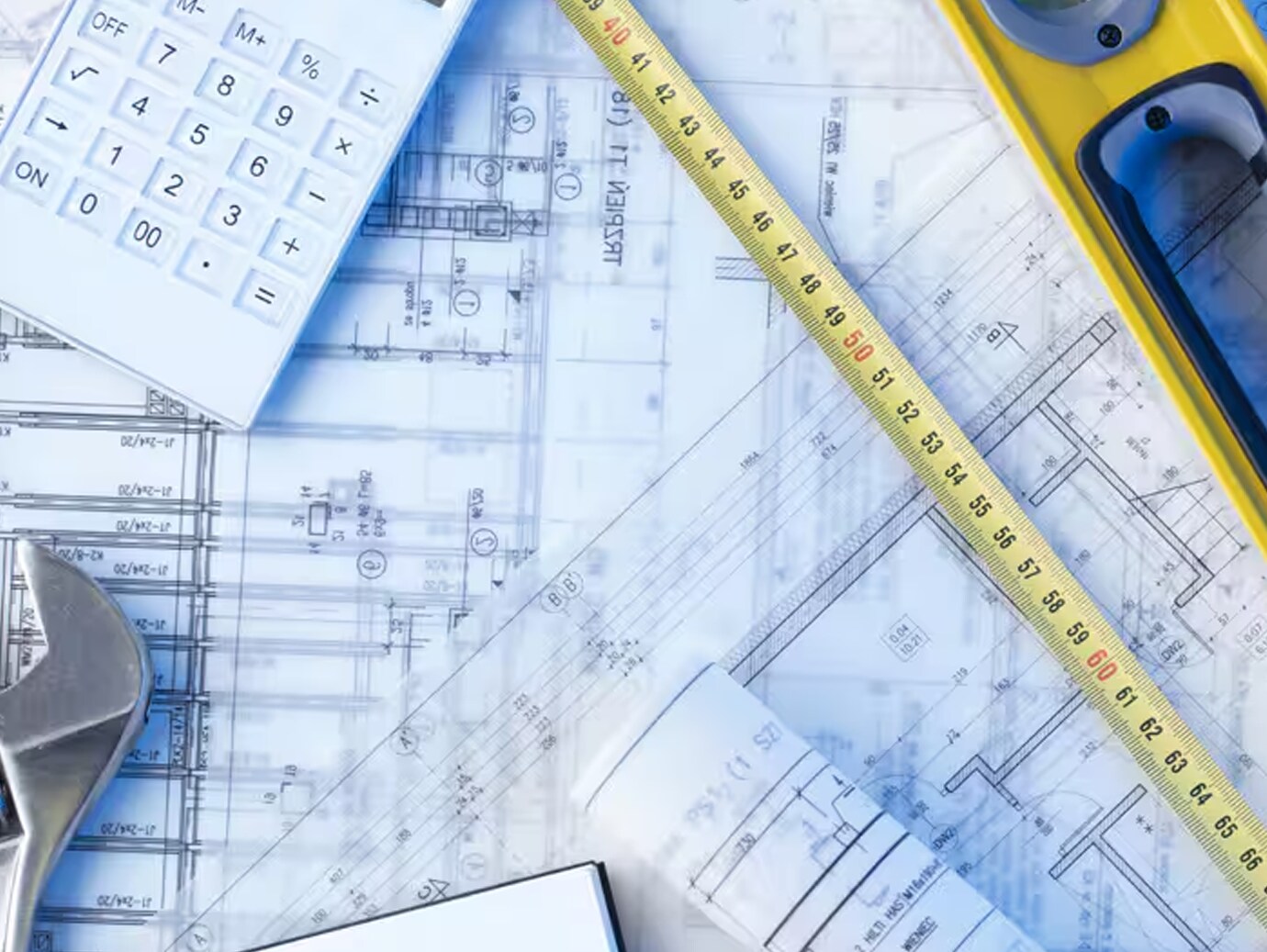 Close-up of a set of architectural blueprints, with a measuring tape and calculator