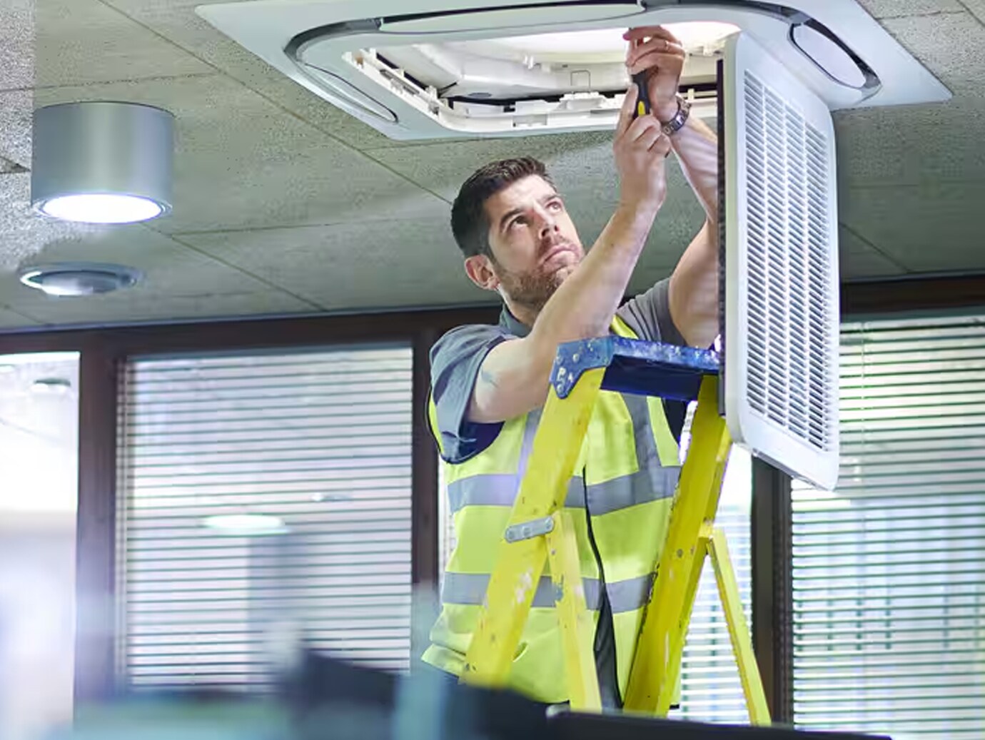 An electrician repairing a light fixture in an office