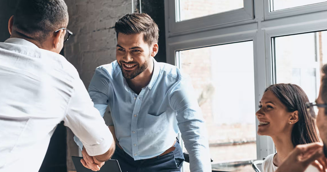 Two employees shaking hands and two others looking at them
