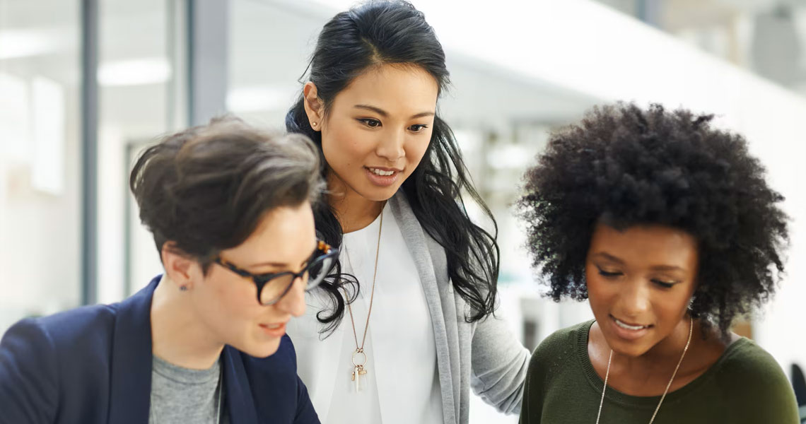 Three women looking at a laptop on a conference table