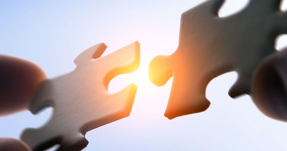 Two hands holding up two puzzle pieces towards the sky