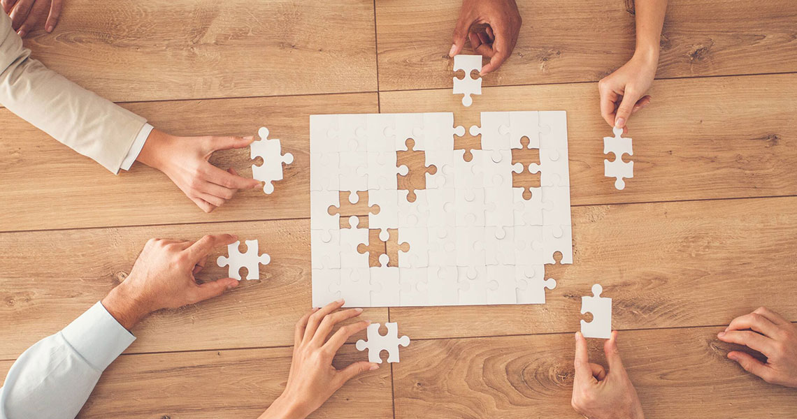 People holding puzzle pieces over a puzzle on a wooden table