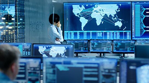 A man looking at maps displayed on a screen, surrounded by computers