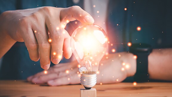 A man holding a lit-up lightbulb on a table