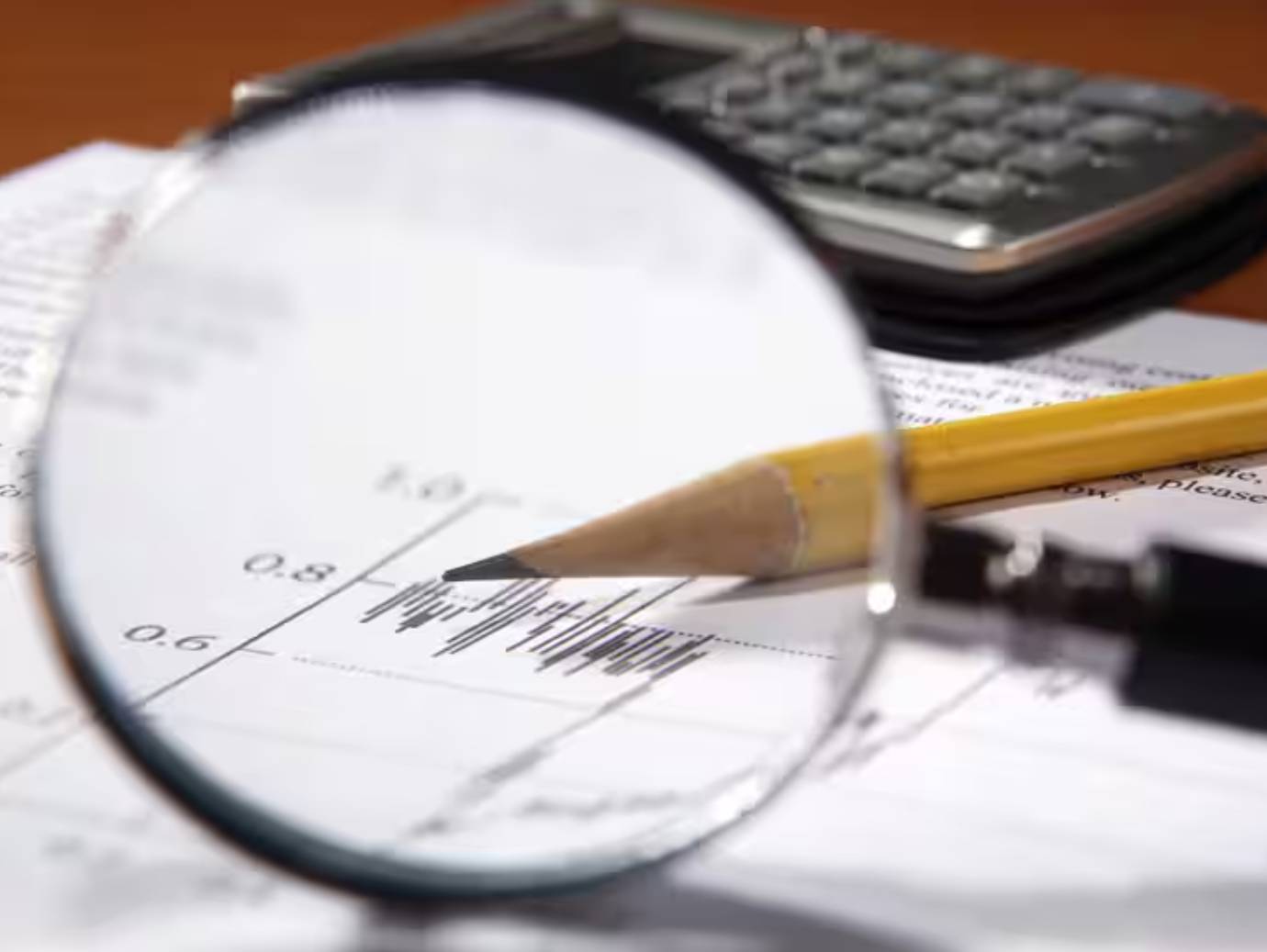 Close-up of a magnifying glass before a document, HB pencil and calculator