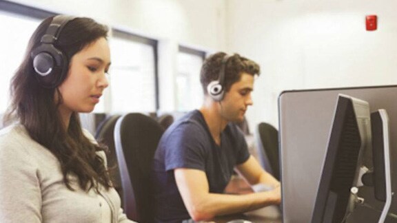 Man and woman wearing headphones and using desktops in office
