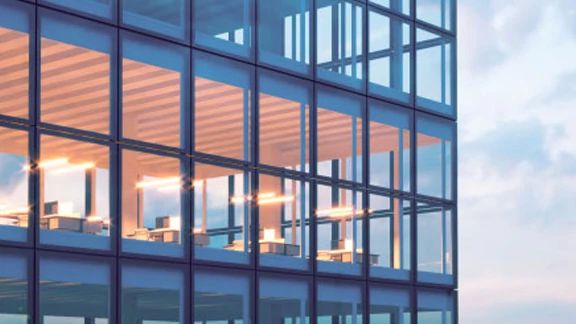 Close-up of an office building with glass windows, with cublices visible through the glass