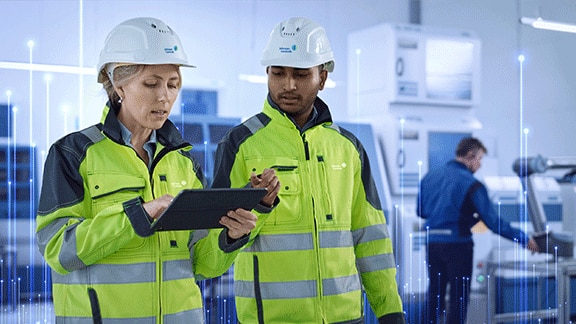 Two engineers wearing protective gear, with one of them looking at a tablet