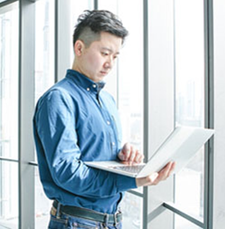 Man standing in front of a window, working on a laptop he's holding